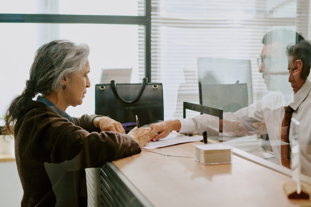 Woman signing documents at a service counter while staff member assists