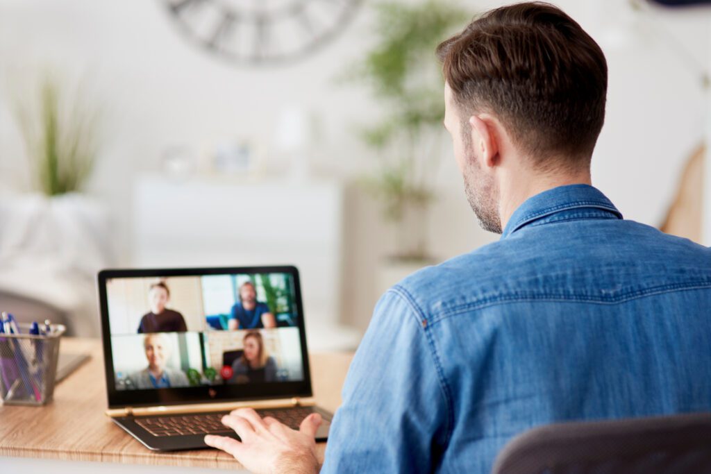 A professional video conference in progress on a laptop screen within a home office environment.