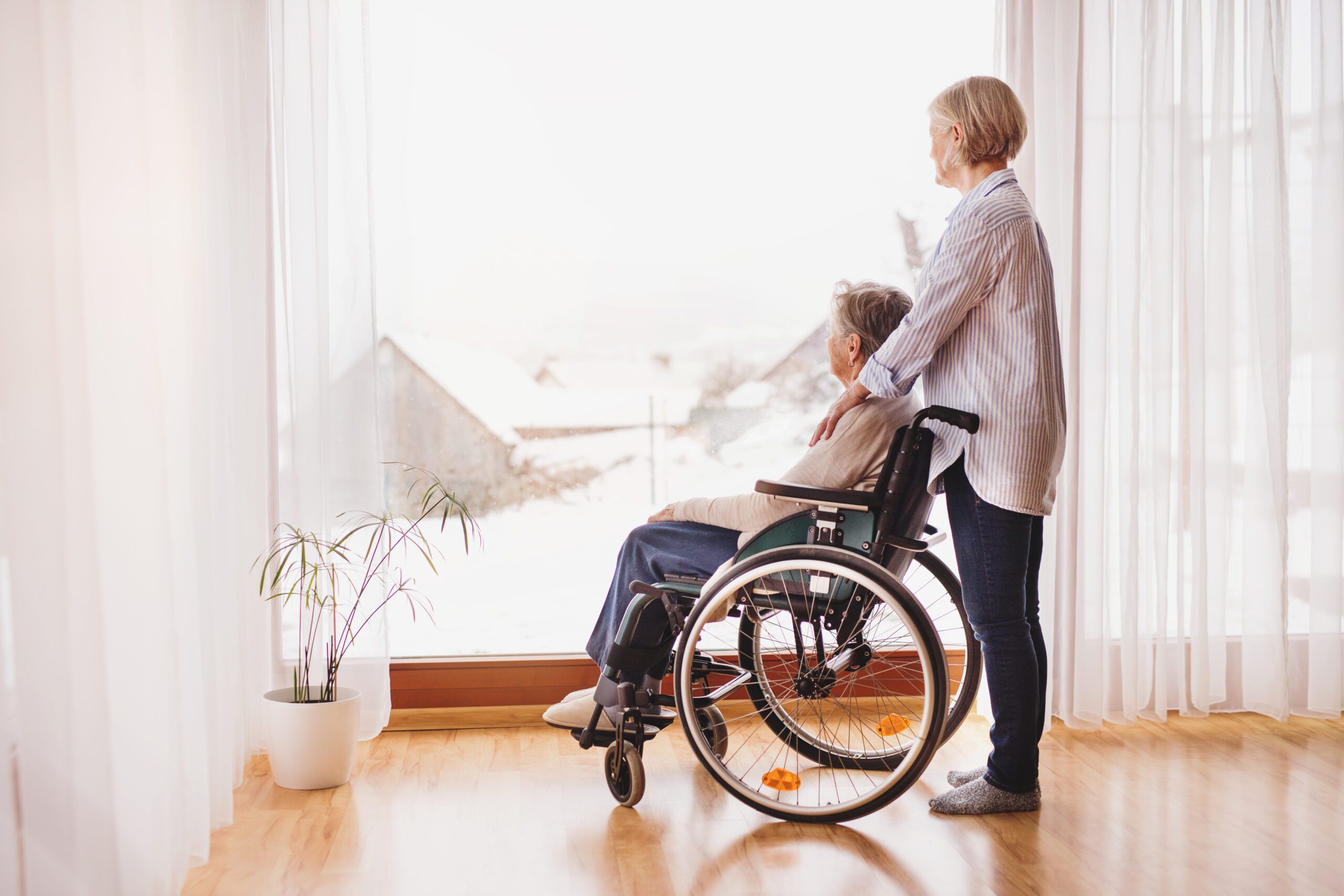 Adult daughter assisting an elderly woman in a wheelchair at home.
