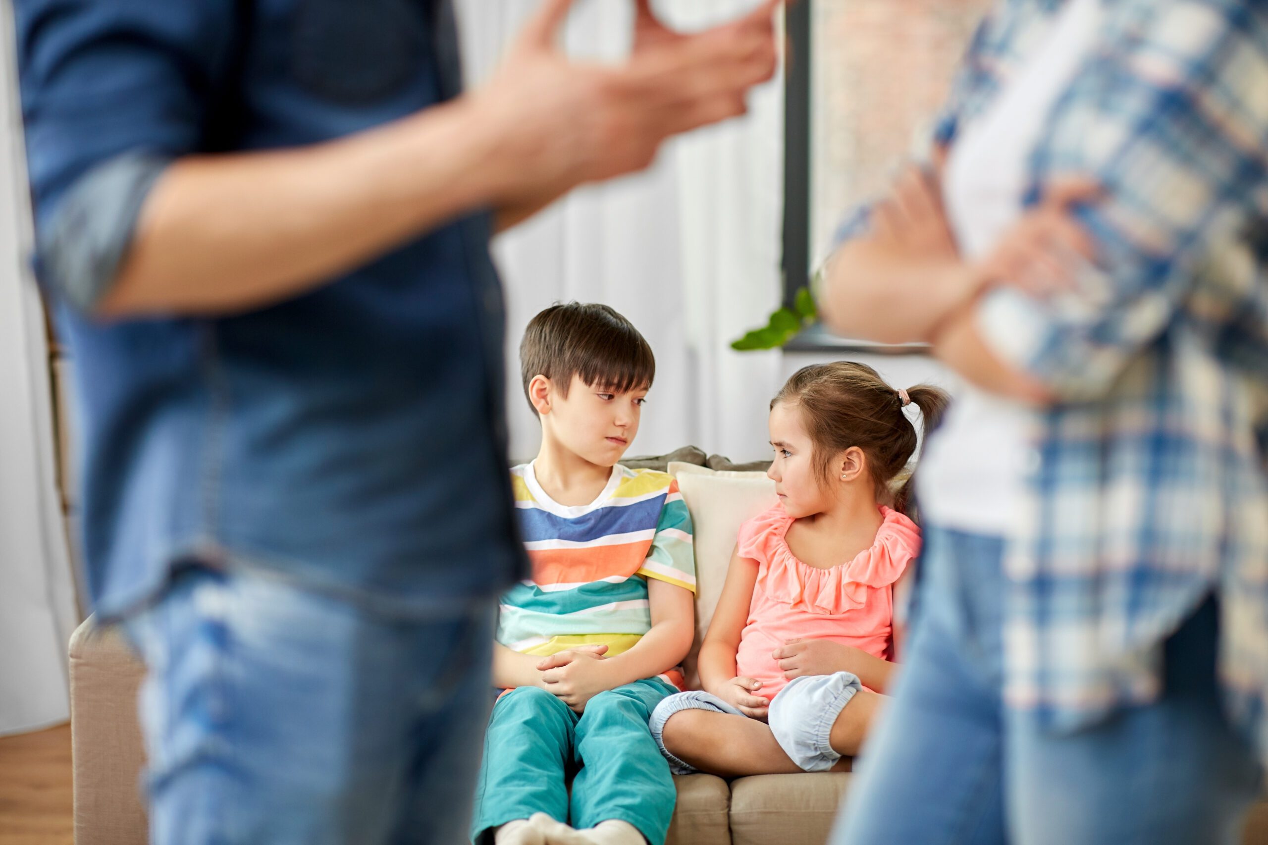 Young children watching from the sofa as their parents face each other in a disagreement.
