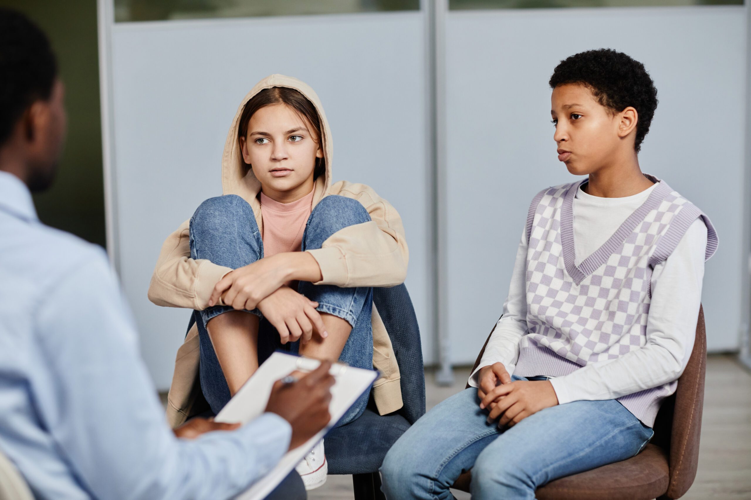 Two teenage girls sitting and speaking with a therapist during a court-referred family evaluation session.