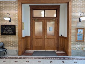 The double-door entrance to the law library from the courthouse hallway, featuring a historical plaque honoring attorney Fred G. Minnis Sr.